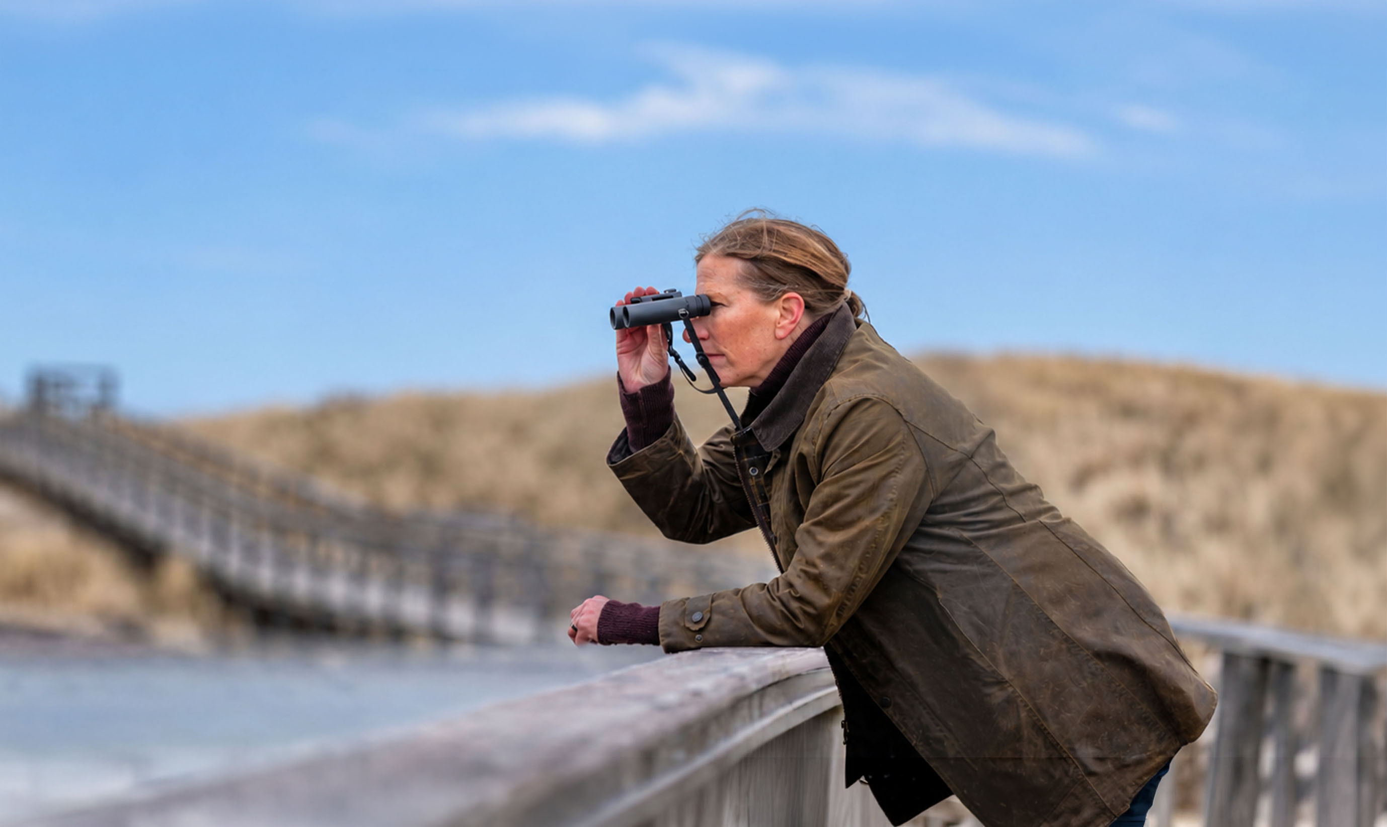 Promotion optique EuroBirdwatch 2026 - Femme regardant dans des jumelles sur un ponton au bord de mer