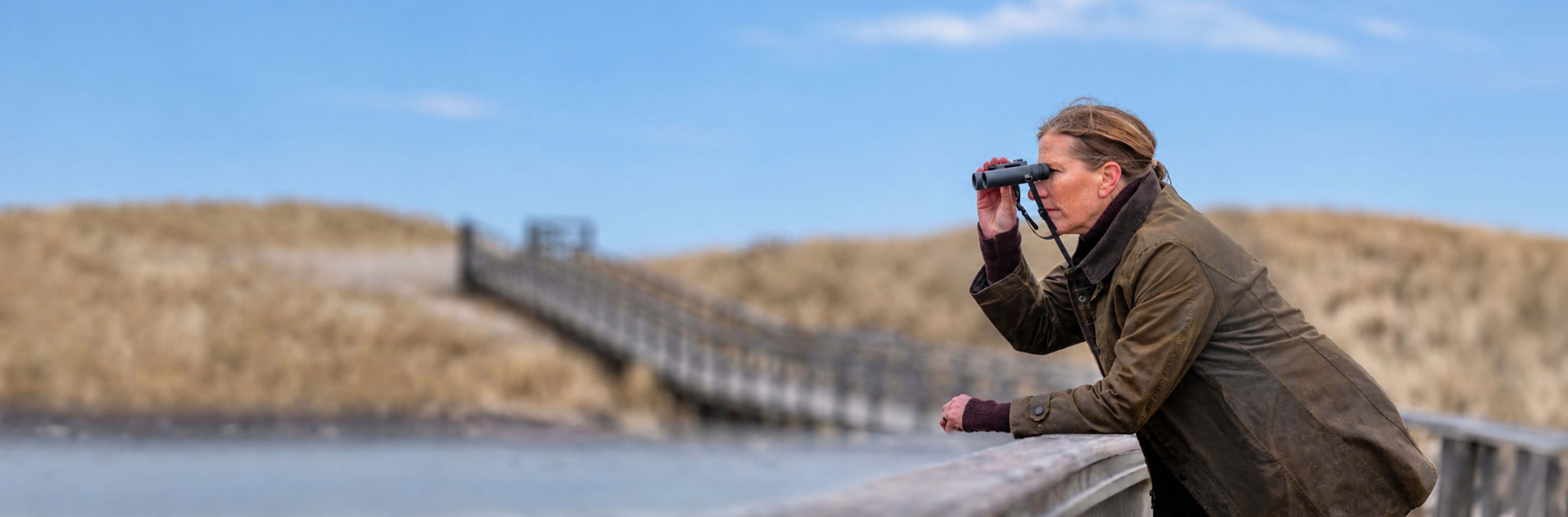 Promotion optique EuroBirdwatch 2026 - Femme regardant dans des jumelles sur un ponton au bord de mer